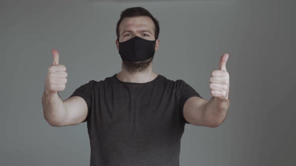 A Man Shows Thumbs Up Wearing a Black Mask alt