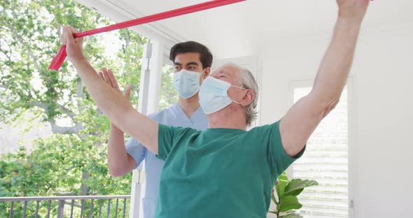 Male therapist and senior man wearing face masks while exercising at nursing home during covid alt