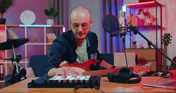 Bald Bearder Pushing Buttons on Drum Midi Player and Playing on the Guitar Together with Drum sounds alt