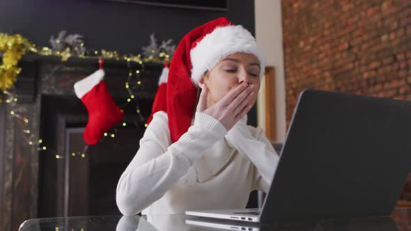 Woman in Santa hat blowing a kiss while having a video chat on laptop at home alt