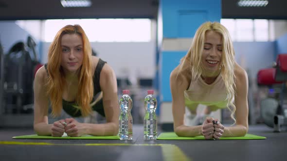 Two Cheerful Motivated Young Caucasian Women in Plank Position Smiling Looking at Camera alt