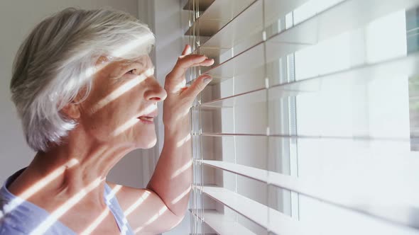 Senior woman looking through the window 4k alt