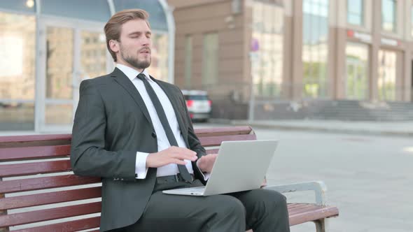 Businessman with Headache Using Laptop While Sitting Outdoor on Bench alt