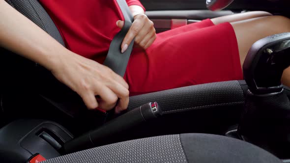 Woman in Red Dress Fastening Car Safety Seat Belt While Sitting Inside of Vehicle Before Driving alt
