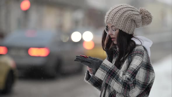 Young Woman Is Recording Voice Message on Smartphone Standing Outdoors in Big City at Winter Day alt