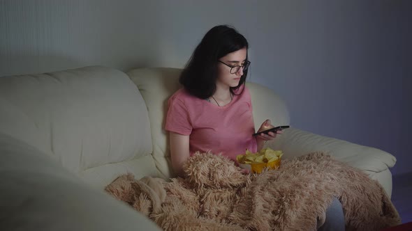 Girl in the Evening on the Couch Near the TV Uses the Phone
