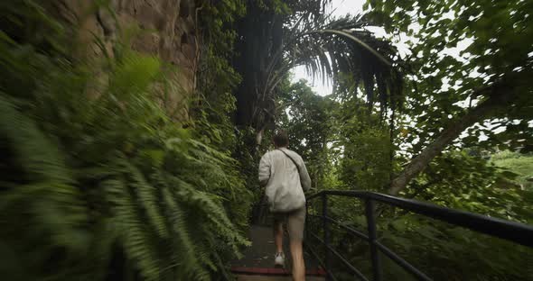 Handheld Tracking Shot of a Young Male Traveler Running on the Stairs Through the Tropical alt