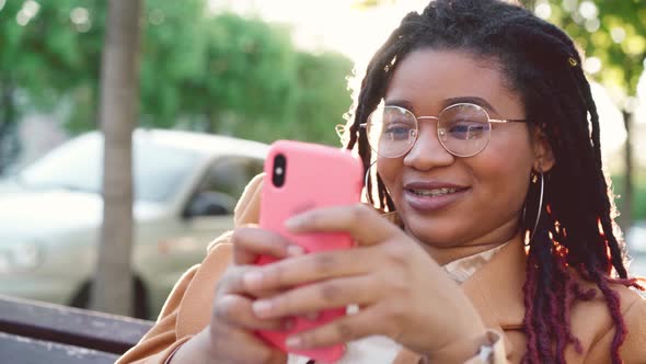Young African American Woman Sitting on a Bench in the City and Using Her Smartphone