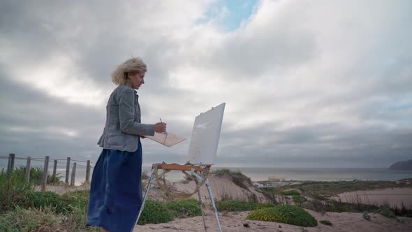 Middleaged European Woman Artist Paints a Seascape with an Original View of the Sea alt