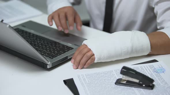 Businessman With Broken Arm in Gypsum Typing on Laptop, Trauma, Workaholics