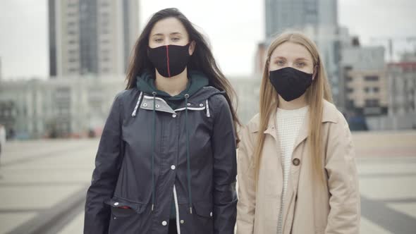 Two Confident Young Caucasian Women in Covid-19 Face Masks Turning To Camera and Showing No Gesture alt