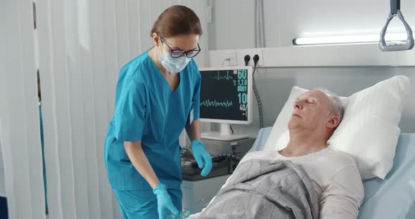 Nurse Putting Oxygen Mask on Senior Male Patient Lying in Hospital Bed alt