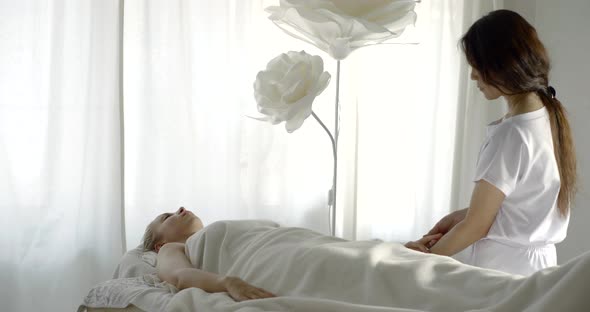 Woman Is Relaxing Lying on Massaging Table in Salon, Asian Master Is Kneading Her Hand alt