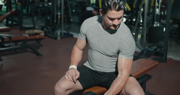 Muscular man guy lifting dumbbell during workout while sitting on bench alt
