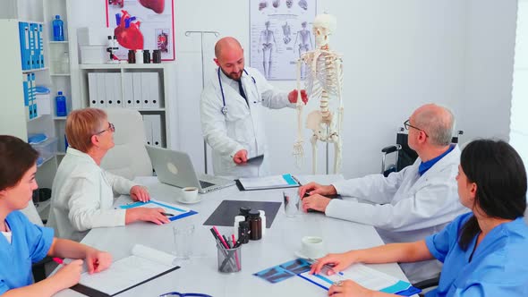 Doctor Explaining Radiography in Front of Medical Staff Using Skeleton alt