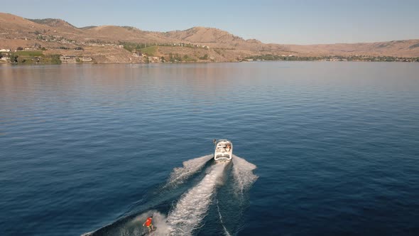 Drone Video Of Boat Taking Off Pulling Up Wakeboarder On Scenic Lake alt