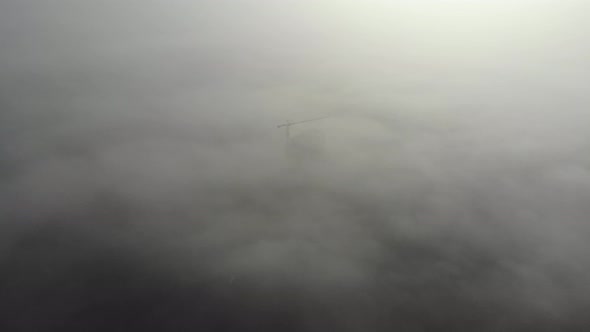 Birds eye view on tower crane in fog standing next to residential building. alt