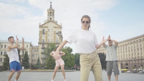 Camera Approaches To Cheerful Young Girl Dancing Robot Dance on Sunny City Square with Group of alt