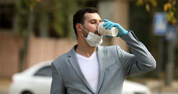 Businessman in medical mask walking the city street with coffee and talking on mobile phone.
