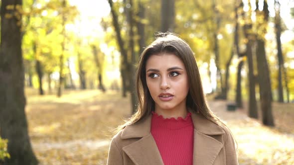 Portrait of Brunette Admires the Nature of Autumn Park with Light Smile alt
