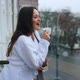 Beautiful young girl in a snow-white terry bathrobe on a balcony with the cup of tea in the morning. - VideoHive Item for Sale