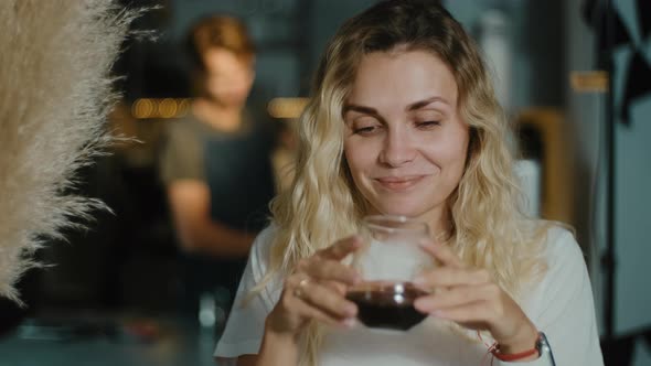 Young blonde woman using laptop browsing online against working barista in a coffee shop alt