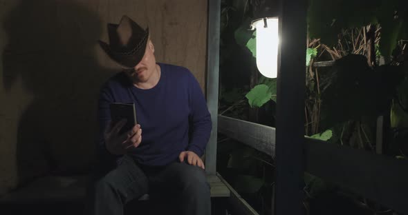 Cowboy Man Communicates Online Using His Phone While Sitting on Porch