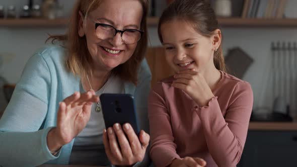 Caucasian grandmother and granddaughter using mobile phone in the kitchen. alt