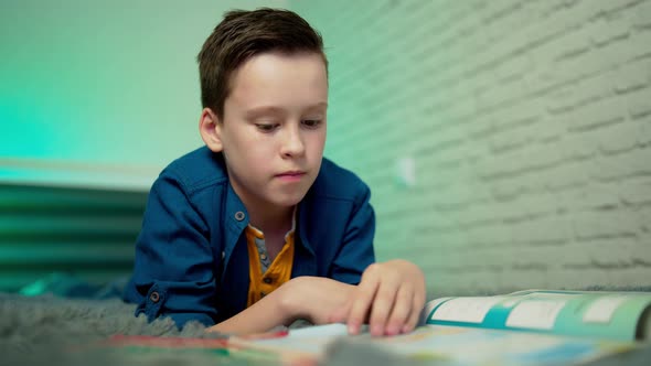 Little boy lying on bed reading book at home alt