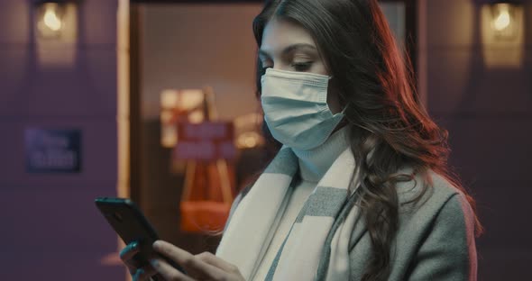 Young woman in the city street wearing a surgical mask and connecting with her smartphone