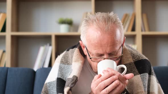 The Old Sick Grandfather Drinks Tea Wrapped in a Blanket Looking Away alt