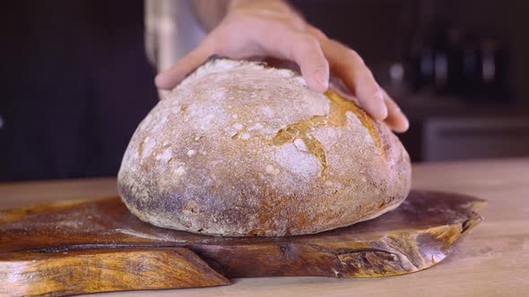 Man Slicing Fresh Home Baked Sourdough Bread In The Kitchen - close up, slider left shot alt