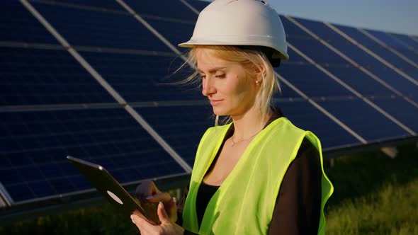 Portrait of a Blonde Female Solar Engineer Standing Uses a Tablet and Looking Away
