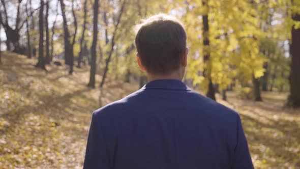 A Middleaged Handsome Caucasian Man Walks and Looks Around in a Park in Fall  Rear Closeup