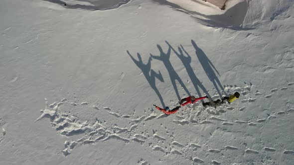 Four Travelers Dance and Show Different Funny Figures Reflecting a Large Shadow on the White Snow