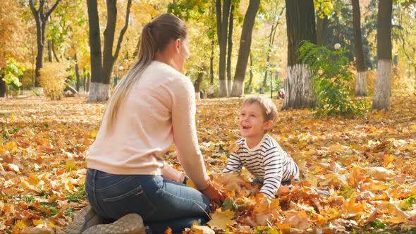  Video of Cheerful Happy Boy with Mother Sitting at Autumn Park and Throwing Up Golden Leaves alt