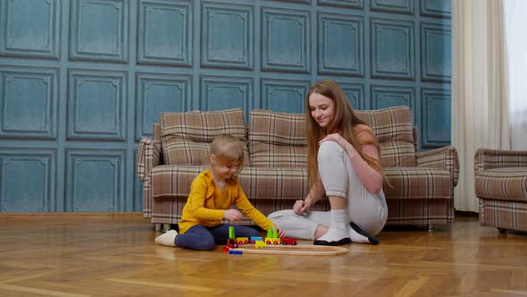 Mother with Little Daughter Child Girl Riding Toy Train on Wooden Railway Blocks Board Game at Home alt