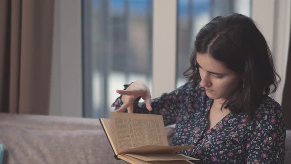 Portrait of a Girl Student Reading a Book While Sitting on the Sofa alt