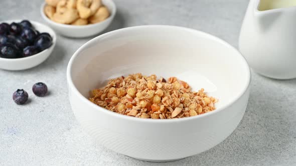 Pouring milk in bowl with muesli cereals breakfast on white background. Granola with nuts and berrie alt
