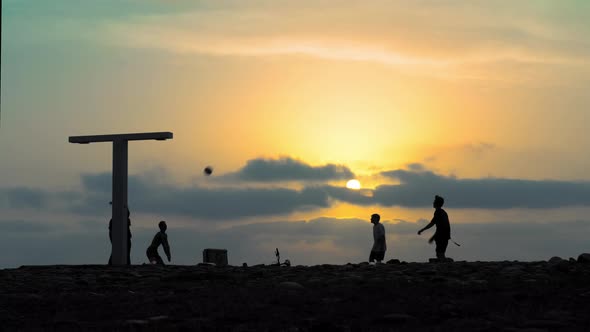 Silhouette of active young people playing volleyball against backdrop of sky by sea alt