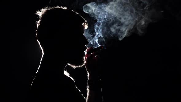 Brutal Man Smokes a Cigar. Takes a Big Drag and Puffs Smoke. Blacklight. Silhouette. Close Up. Slow alt