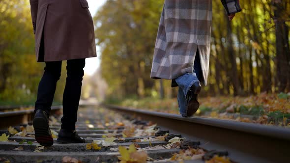 Women's Feet Walk on the Rail Men's on the Sleepers Against the Background of Autumn Trees alt