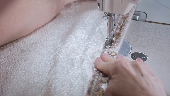 Footage of a woman sewing a white cotton with a sewing machine