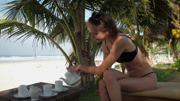 Nice Lady Smiles and Pours Tea in Cup Sitting on Sunbed alt