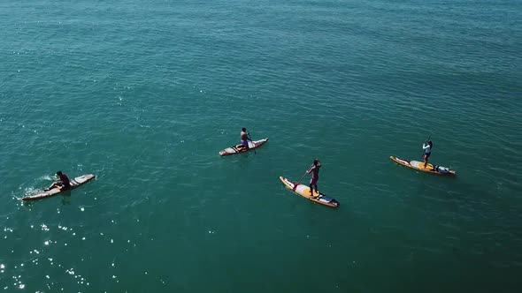Drone circling around group of paddlers on crystal clear light blue water alt