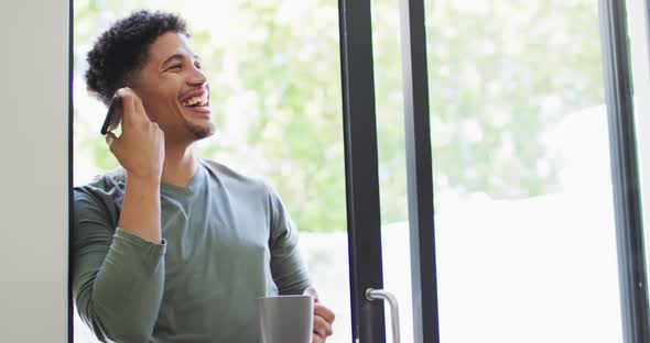 Happy biracial man talking on smartphone and drinking coffee alt