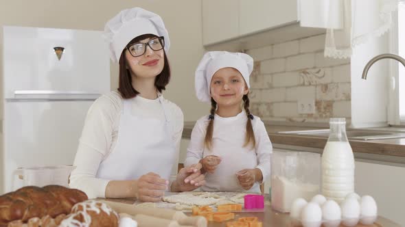 Cute Happy Caucasian Girl and Her Mother in White Hats of Chef and Aprons with Flour on Faces alt