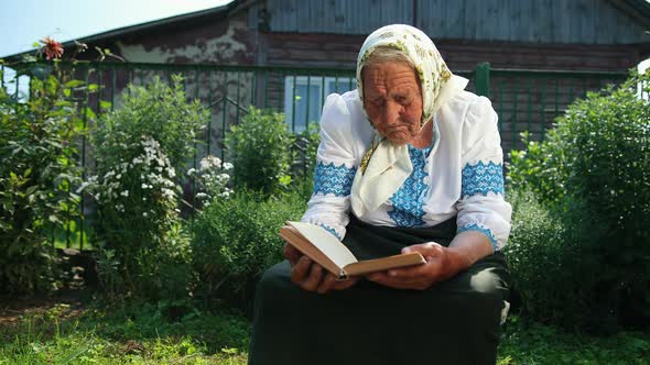 An Old Grandmother is Sitting on the Street and Reading a Book alt