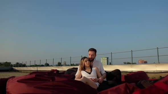 Young Caucasian man and girl are sitting on  roof of a building on soft sofas alt