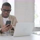 African Man Using Smartphone While Using Laptop in Office - VideoHive Item for Sale